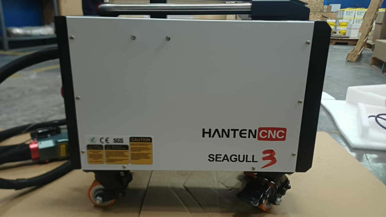 Máquina de limpieza láser portátil HantenCNC Seagull 3, vista frontal con etiquetas de certificación, sobre cartón en un almacén