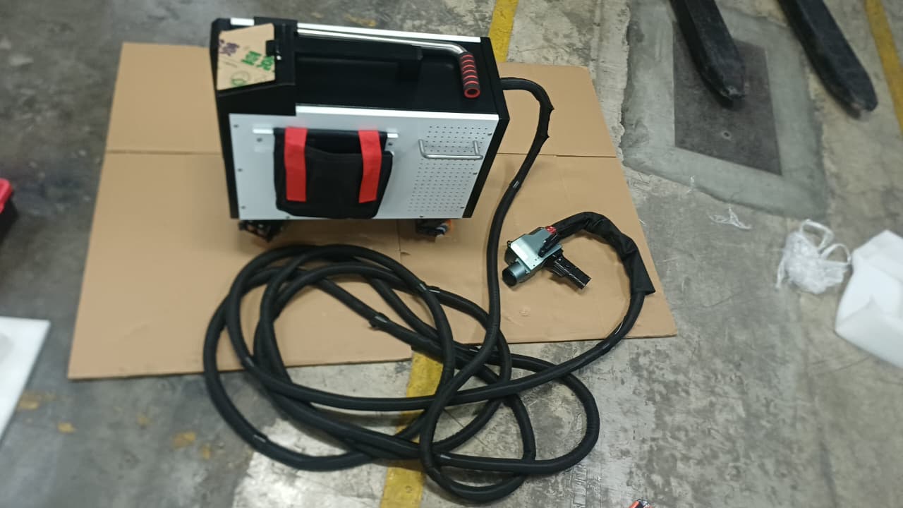Máquina de limpieza láser vista desde arriba, junto a su pistola manual y el cable extendido sobre el piso